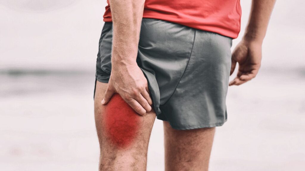 A person in athletic wear holds their thigh, which is highlighted in red, indicating pain or injury