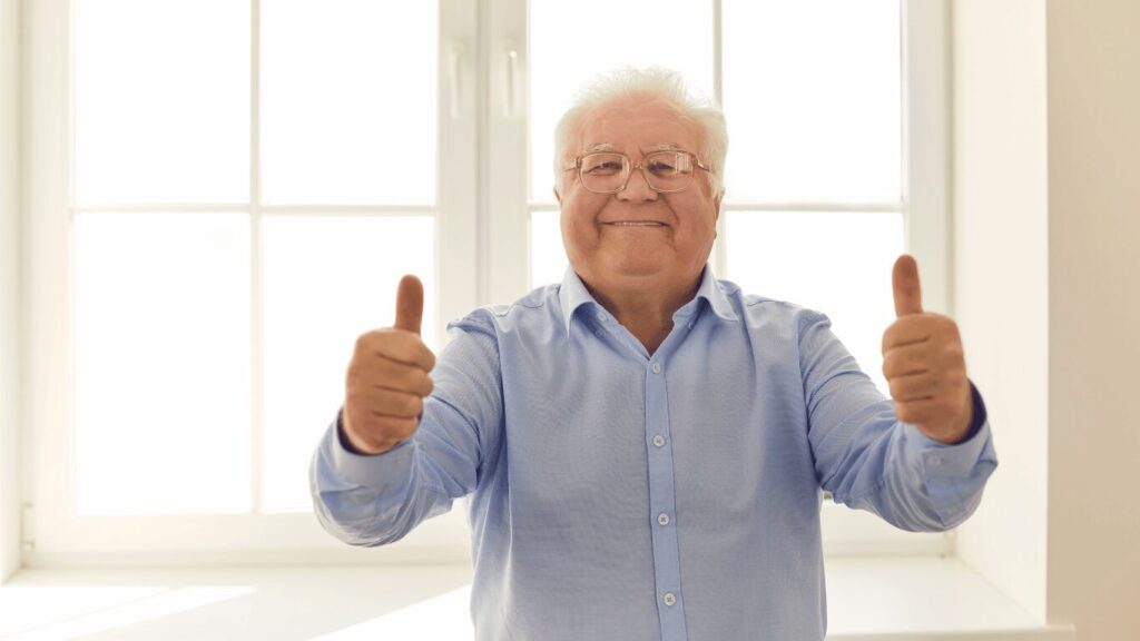 A man wearing a blue shirt and glasses gives two thumbs up while smiling